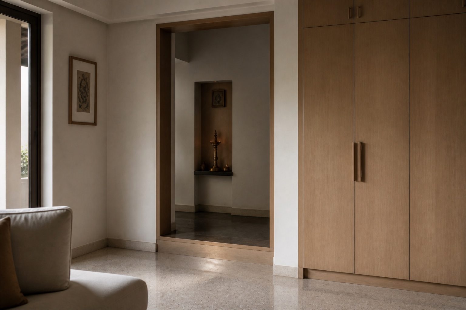 View from a living room toward a recessed prayer niche, timber reveal and stone floor marking the threshold, joinery closed
