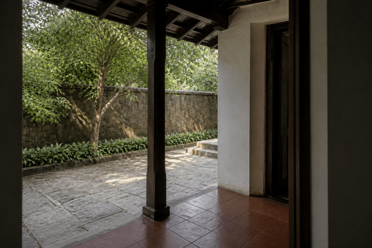 Small Indian courtyard seen from inside, with a stone floor continuing toward a planted edge and a deep reveal