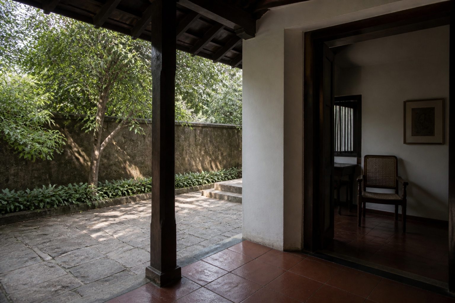 Shaded Indian verandah looking onto a stone courtyard with a single tree, the interior held back by timber posts and a deep reveal